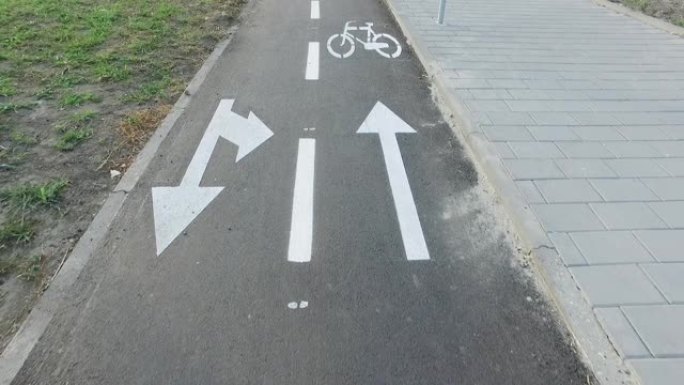 在新的黑色柏油马路上，地面上有涂漆白色自行车标志或符号和箭头的自行车道