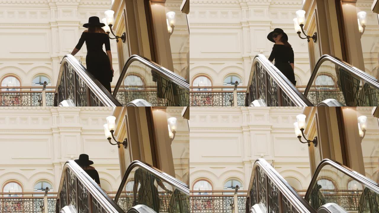 穿着黑色连衣裙的时尚女人走上自动扶梯，转身回头微笑。第一场景概念。慢动作