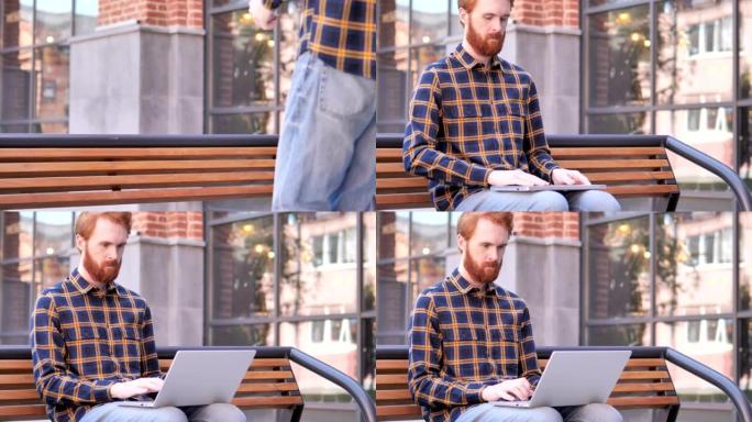 红发胡子年轻人过来坐在长凳上使用笔记本电脑