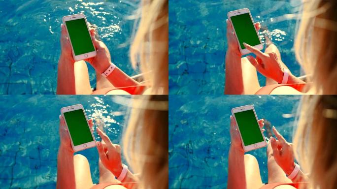 女孩在游泳池附近放松时使用垂直手机绿屏。手握智能手机铬键，手指点击现代显示智能手机，滚动功能信息