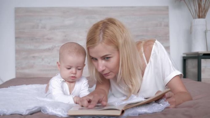 有爱心的妈妈带着书给她的小女儿读童话故事，然后亲吻她躺在家里的床上
