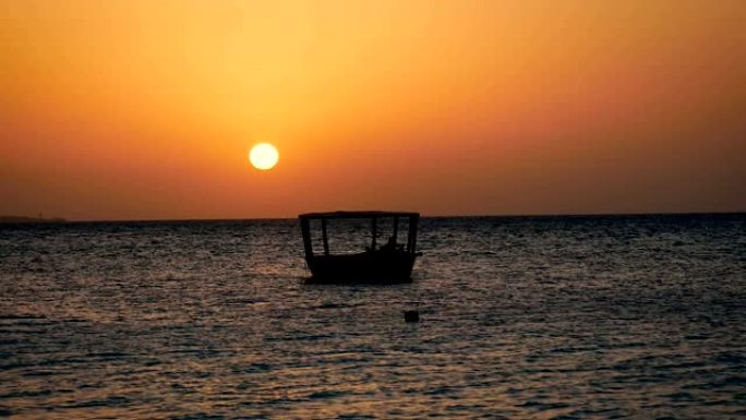 渔船的黑色剪影在日落时大红太阳的海浪上摆动