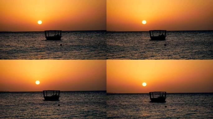 渔船的黑色剪影在日落时大红太阳的海浪上摆动