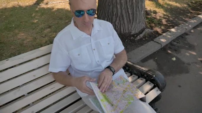 一个穿着白衬衫的中年男子坐在长凳上，正在研究纸质地图