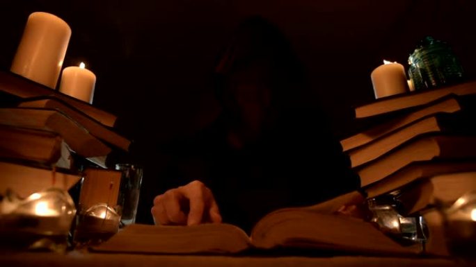 中等特写女孩魔术师在烛光下的黑暗房间里的兜帽里，寻找翻书的咒语。低调。