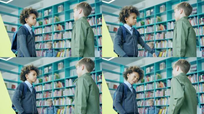 两个男小学生朋友，混血和高加索男孩，在学校图书馆的书架旁站着友好的谈话