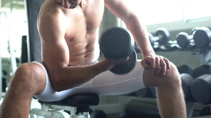 运动员的肌肉手臂在做哑铃卷发，男人在健身房一次锻炼肌肉一个代表强壮的二头肌。
