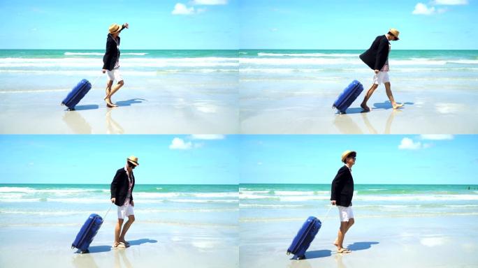4k景观侧视图跟踪拍摄年轻的亚洲商人游客携带蓝色行李，在沙滩上漫步，天空背景为海浪和云。商人在海滩度