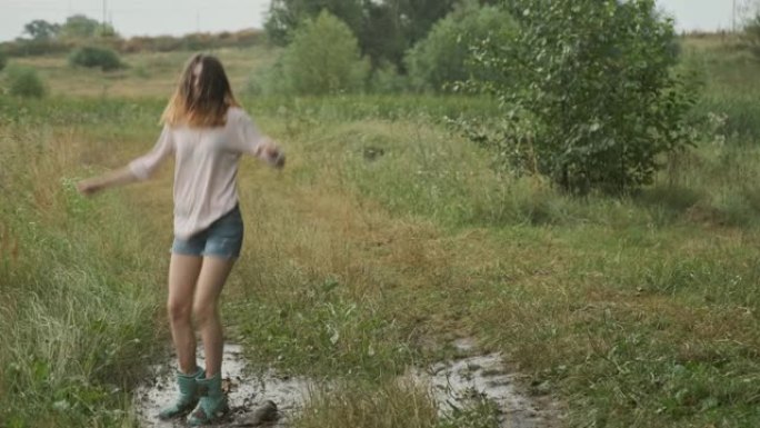 美丽微笑的少女跳进乡村道路上非常泥泞的水坑，雨后的夏天自然背景
