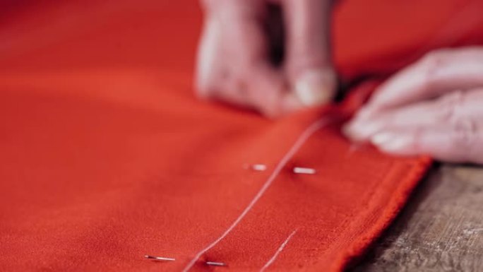专业女裁缝将别针放入桌子上的红色织物中。