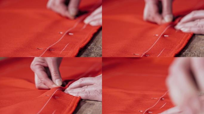 专业女裁缝将别针放入桌子上的红色织物中。
