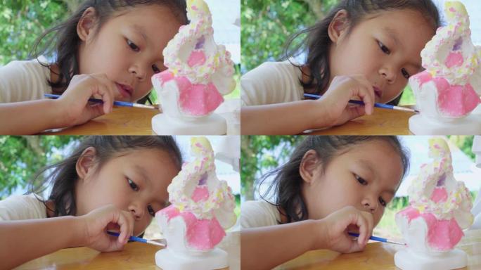 亚洲小女孩集中精力用画笔画洋娃娃石膏。