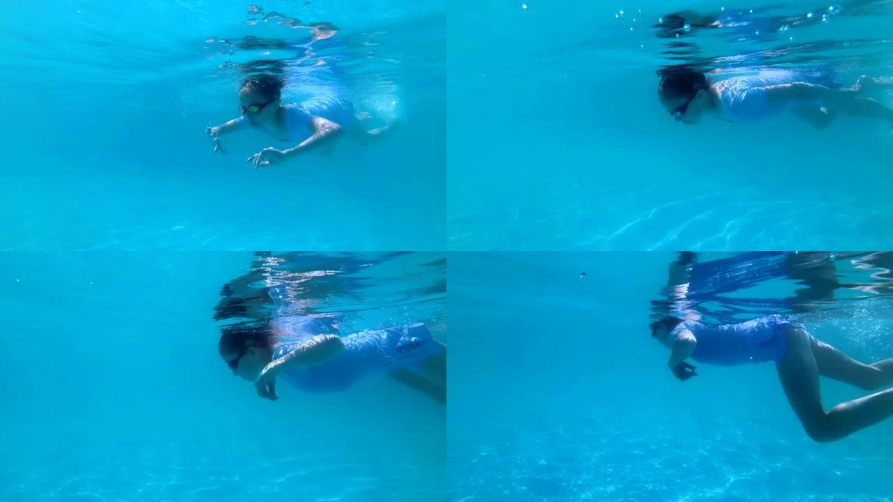 一个甜美的年轻女孩在室外游泳池里从事运动，在阳光明媚的日子里，穿着蓝色泳衣和红色眼镜在水下游泳。特写