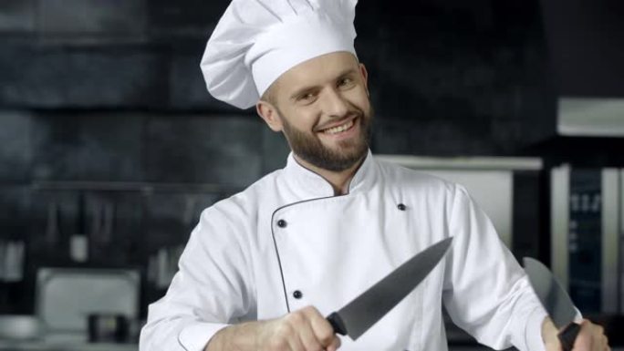 男厨师在厨房玩刀子。微笑的厨师磨十字刀