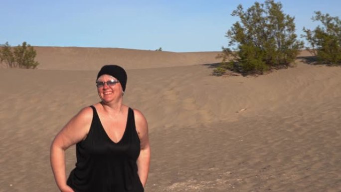 成熟、身体积极的幸福女人在加州死亡谷梅斯基尔公寓的沙丘上徒步旅行。