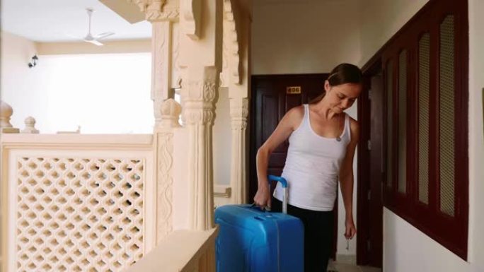 女人走进旅馆，把手提箱卷到她的房间。前视图。