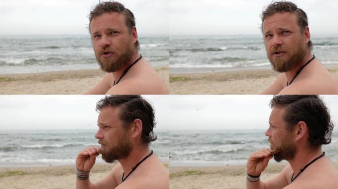 一位在大海背景上留着胡须的年轻人正在用木梳子梳理胡须。4 k视频