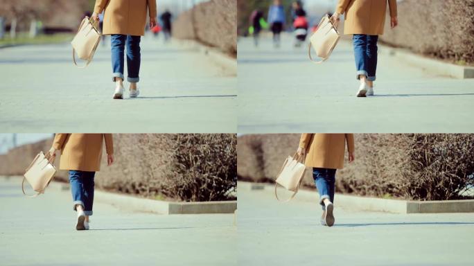 女人穿着运动鞋和提包沿着公园的小路走。早春散步。底视图和后视图。