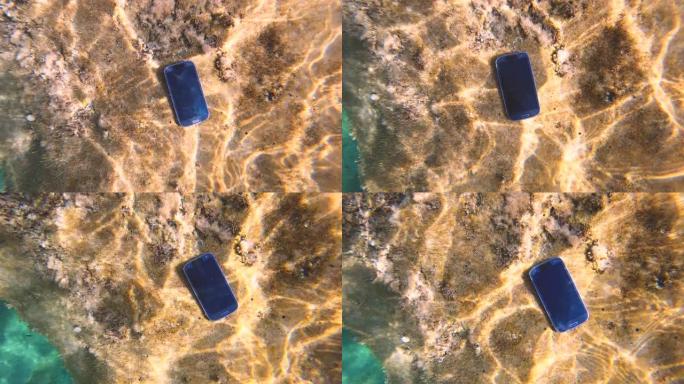 智能手机掉了。手机掉入海床上的海水中的水下镜头。