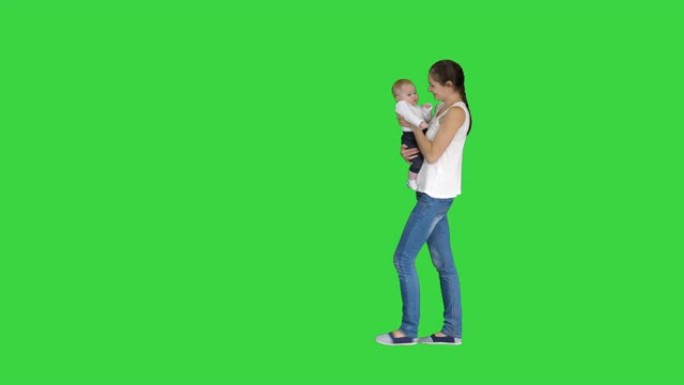 年轻的母亲双手抱着婴儿，走在绿色屏幕上，色键