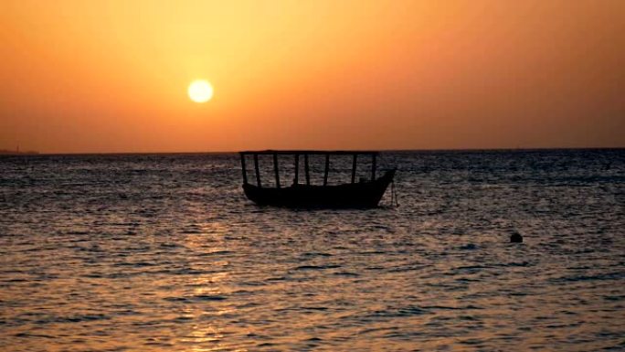 渔船的轮廓在日落时大红太阳的海浪上摆动