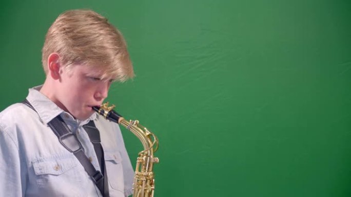 12岁的男孩正在工作室里演奏萨克斯管，背景是绿色色键。