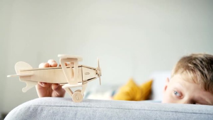 玩木制飞机玩具模型的男孩。他把它 “落在” 客厅沙发扶手上。快乐童年概念慢动作视频。