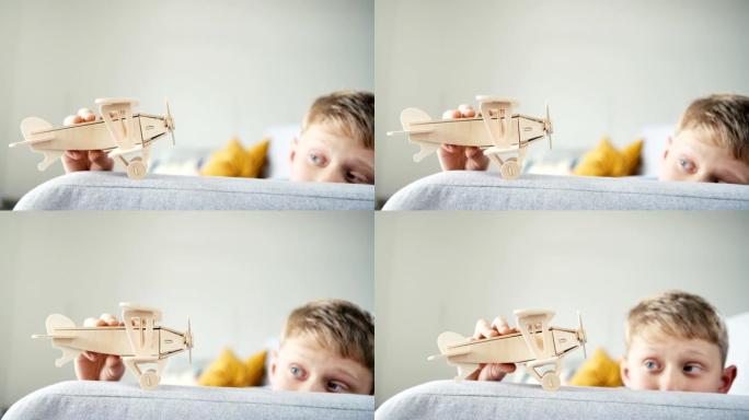 玩木制飞机玩具模型的男孩。他把它 “落在” 客厅沙发扶手上。快乐童年概念慢动作视频。
