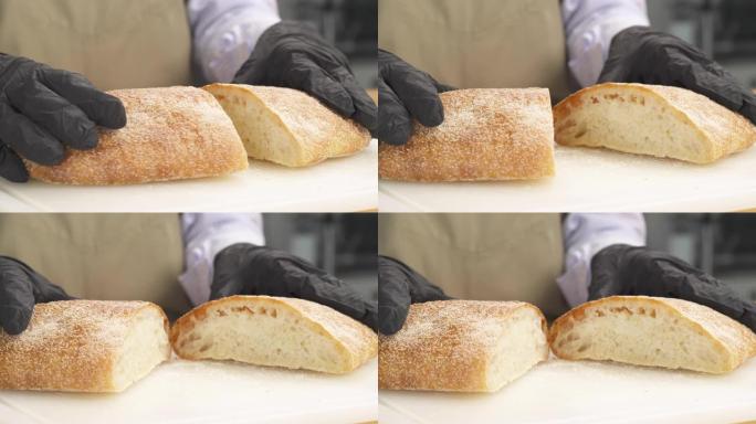 专业厨师的特写镜头将新鲜出炉的ciabatta面包切成两部分，并展示了面包的质量。孤立的，在木质表面