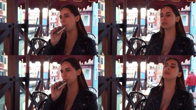 在咖啡馆的阳台上用烟草加热器吸烟的女孩
