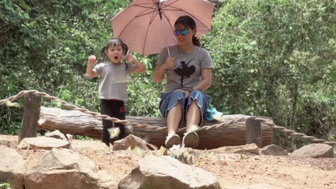 亚洲年轻的母亲和小女儿看着大自然中的蝴蝶，妈妈和小朋友们玩得开心快乐，孩子们学习自然，幸福的家庭观念