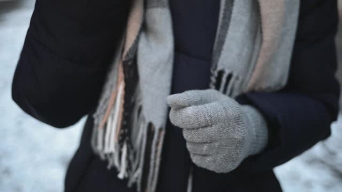 特写女人的手从口袋里拿口红，在冬天站在城市的白雪皑皑的街道上涂抹在嘴唇上。