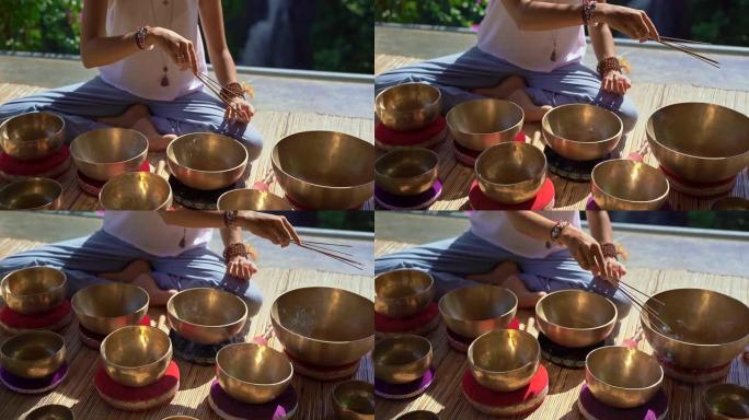 一位亚洲神圣医学大师的超低镜头表演了西藏碗愈合仪式。用藏族歌唱碗冥想。她坐在凉亭里冥想，背景是美丽的