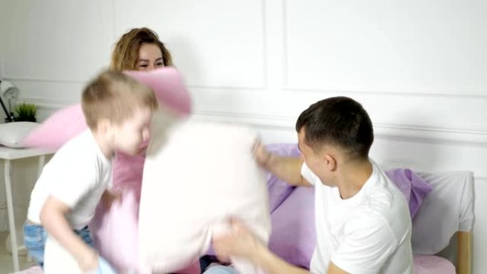 年轻的家庭: 爸爸妈妈和小儿子在床上玩枕头大战。
