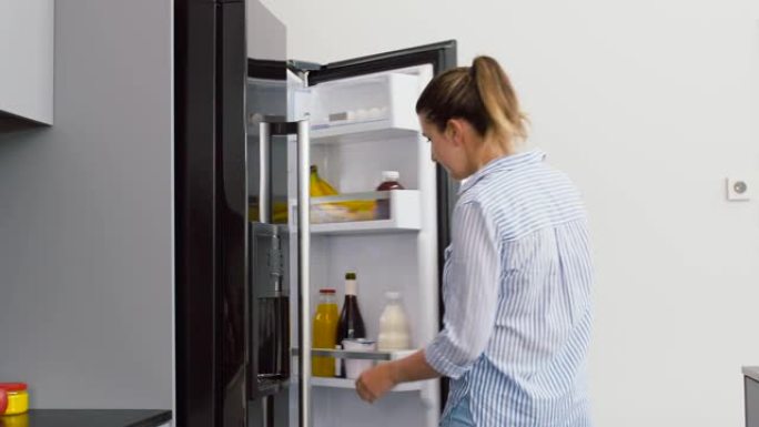 女人从家庭厨房的冰箱里取果汁