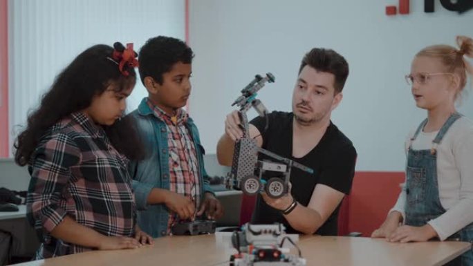 混合种族的学童控制机器人机器与遥控老师在一起。在学校从事技术项目的创意孩子