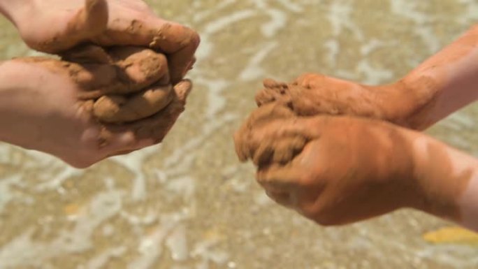 双手在沙滩上制作粘土的特写镜头，沙子和波浪作为背景，夏天和旅行概念。