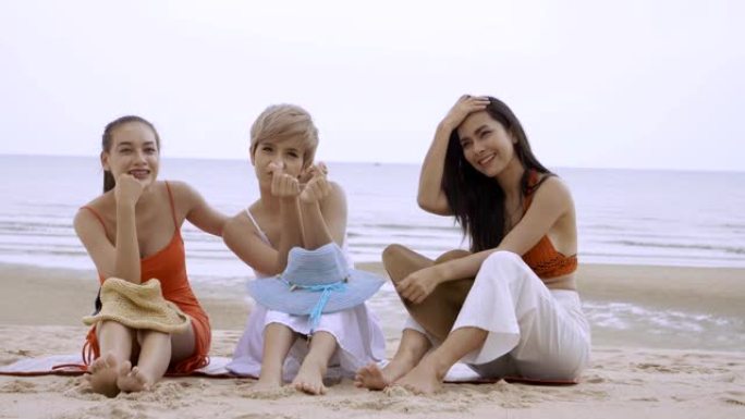 三个亚洲女性性感女孩坐在沙滩上微笑秀迷你心在手