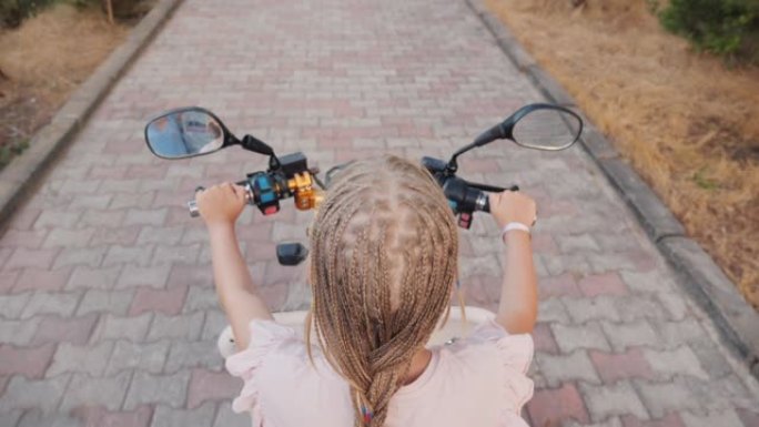 一个非洲辫子的孩子骑着踏板车的俯视图，后视图。开朗积极的娱乐