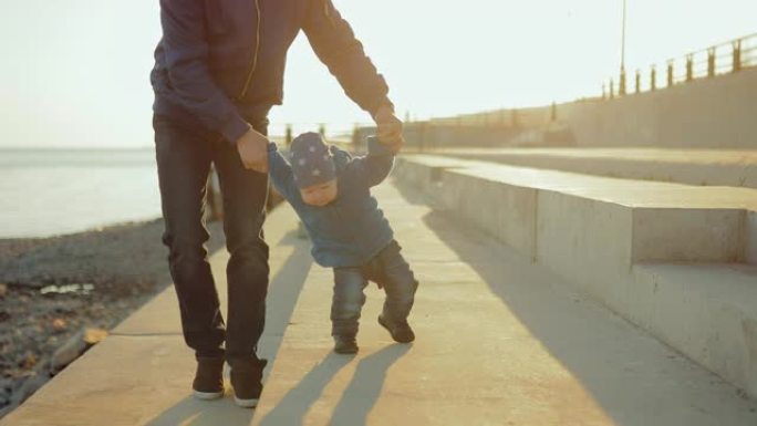 孩子和他爸爸一起抱着胳膊沿着小路走，微笑着。爸爸教他的小儿子走路。快乐的童年。