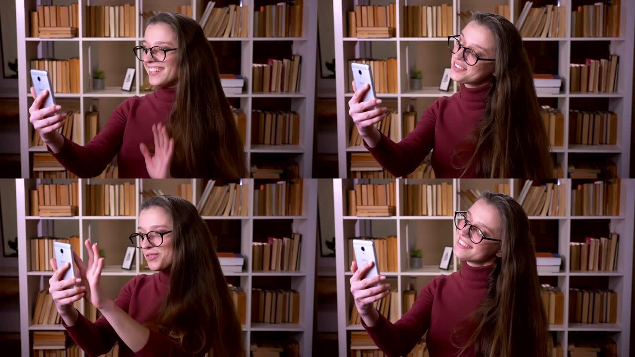 戴着眼镜的年轻高加索女学生的特写肖像在室内的大学图书馆里，在电话上进行视频通话