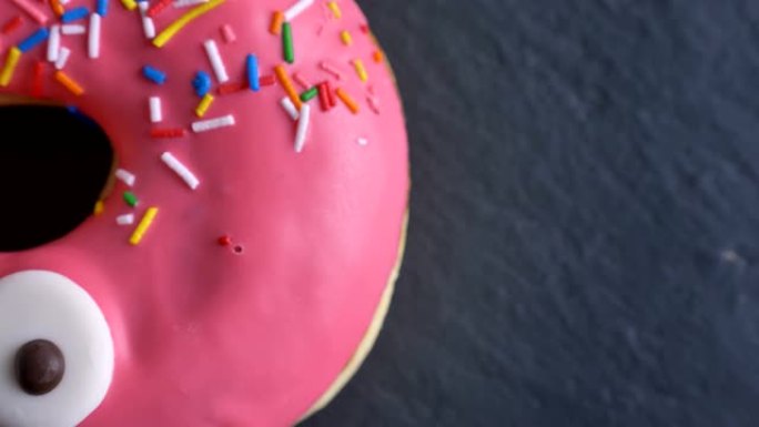 粉红色甜甜圈的特写半镜头，彩色碎屑和眼睛在灰色桌子背景上缓慢旋转。