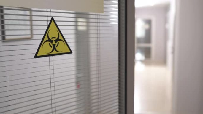 在实验室工作的人。实验室入口门上生物威胁警报的生物危害符号标志