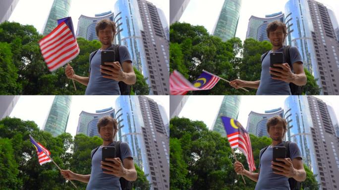 一名年轻人拿着智能手机挥舞着以摩天大楼为背景的马来西亚国旗。去马来西亚旅游的概念