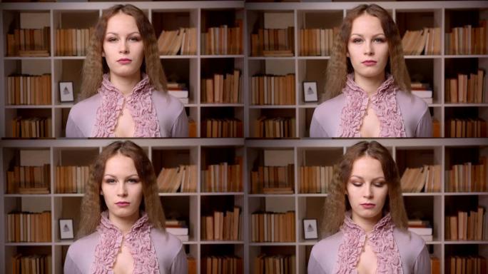 高加索波浪形金发图书管理员的肖像平静地、固定地看着书架背景上的相机。