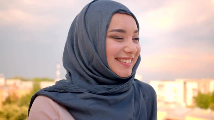 戴着头巾的穆斯林学生的特写肖像，站在阳台上欣赏城市美景，高兴地对着镜头微笑。