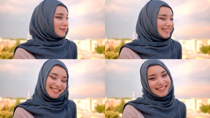 戴着头巾的穆斯林学生的特写肖像，站在阳台上欣赏城市美景，高兴地对着镜头微笑。