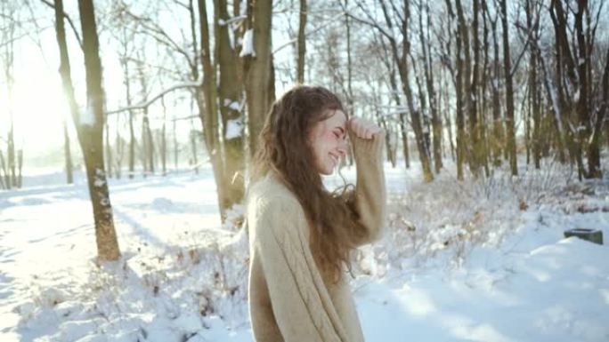 穿着毛衣的迷人年轻女孩在寒冷中玩耍。卷曲的年轻女子穿着暖和的衣服，背景是白雪皑皑的森林。冬季景观。北