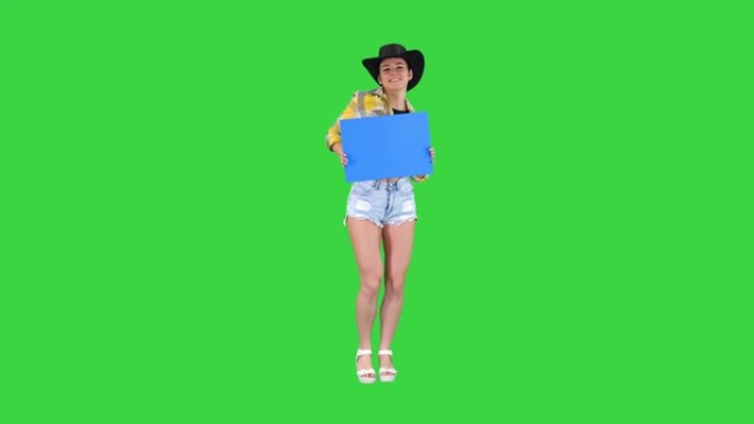 微笑的漂亮女牛仔拿着空木板，在绿色屏幕上跳舞，蓝色模型