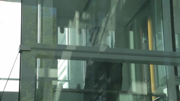 英俊的高加索商人穿着西装下班，从透明的玻璃电梯下来到带有自然倒影的凸窗，商业中心的金融大楼。